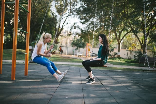 two girls talking after feeling lonely after break up on a park's swing 