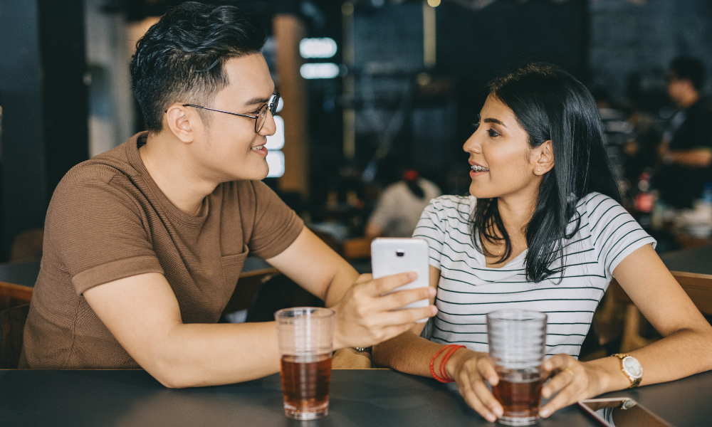 girl sitting down with boyfriend showing something on his phone