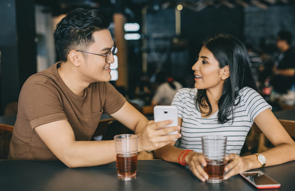 girl sitting down with boyfriend showing something on his phone