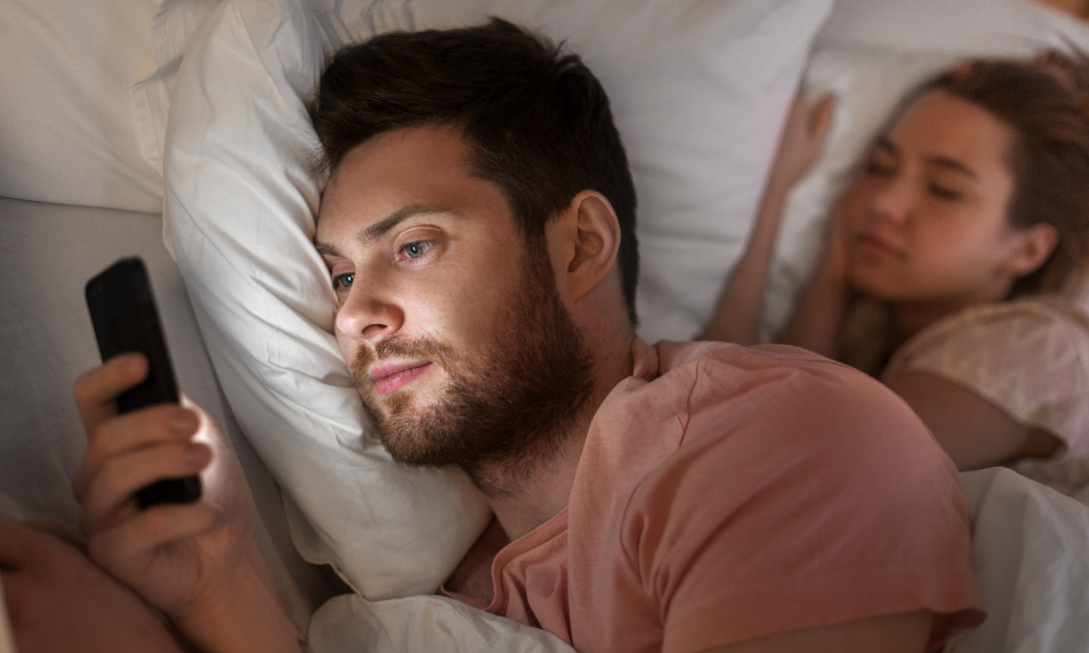 guy talking on the phone while girlfriend is sleeping next to him 